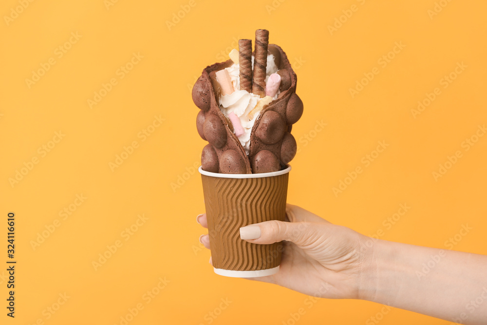 Female hand with delicious sweet bubble waffle on color background