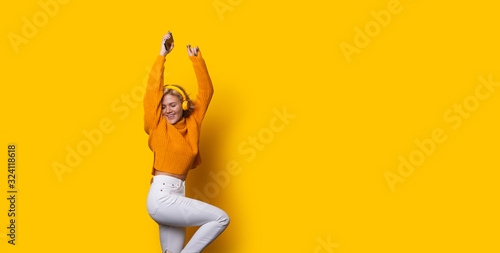 Fotomural Stunning blonde caucasian girl dressed in an orange sweater and white jeans is d