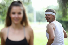 Man Looks Back To Look At Beautiful Figure Girl. Attractive People In Sportswear Running Around Park. Man Likes Figure Slender Girl. Guy Dreams Losing Weight And Having Beautiful Body.