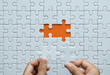 © gballgiggs - Hand putting jigsaw puzzle white color on orange background
