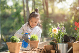 Fototapeta Lawenda - adorable 8 years old asian little girl is watering plant in pots in garden outside house, child education of nature. caring for a new life. earth day holiday concept. world environment day. ecology.