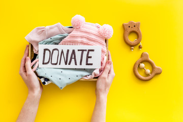 Donate text. Box with clothes for kids - in hands - on yellow background top-down