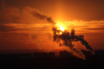 Wall Mural - red sun at sunset or dawn at dusk low above the horizon shrouded in smoke from the chimneys of the p