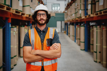 portrait of confident worker wearing helmet and spectacles with orange vest uniform standing in aisl