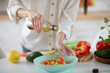 © zinkevych - Hands of a young woman pouring olive oil into a salad.