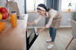 © zinkevych - Young woman in an apron standing leaning towards the oven.