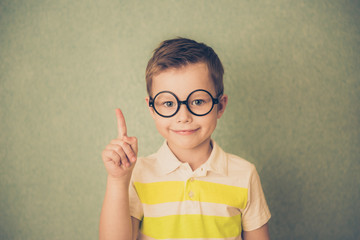 Portrait of stylish little boy with finger pointed up. Kid on blue blackboard. Success, bright idea, creative ideas and innovation technology concept