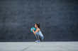 © Dusan Petkovic - Side view of caucasian sportswoman in shape holding weight ball while crouching and doing endurance. In background is dark wall.