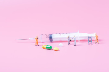 Syringe and miniature human and oral medicine and thermometer macro closeup on pink background