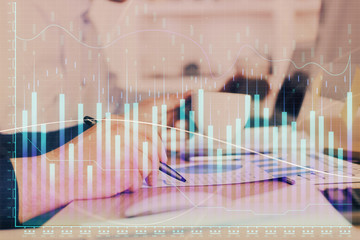 Double exposure of man's hands writing notes of stock market with forex graph.