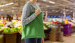 consumerism and eco friendly concept - woman with green reusable canvas bag for food shopping over supermarket on background