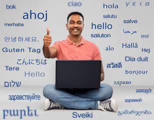 Poster - technology, communication and people concept - happy indian man with laptop computer sitting on floor over greeting words in different foreign languages on grey background