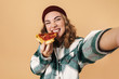 © Drobot Dean - Photo of pretty happy woman in knit hat taking selfie and eating pizza