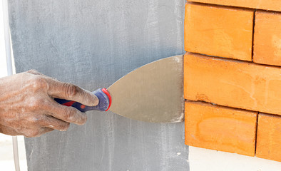 Plastering wall with putty-knife. Close up image man holding putty-knife on cement wall. Fixing wall surface and preparation for painting.