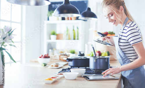 Fotografía Young woman using a tablet computer to cook in her kitchen