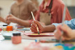 © AnnaStills - Close-up of child holding paintbrush and painting a picture at the table with other children