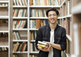 Wall Mural - Smiling korean guy holding textbooks at library