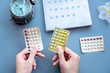 woman hand choosing oral contraceptive pill, with calendar and clock on background 