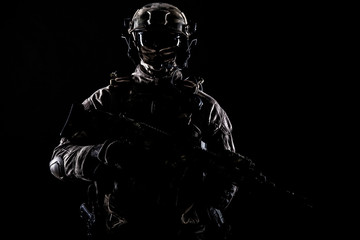 Army special operations forces soldier in mask and combat uniform, armed submachine gun, low key studio portrait on black, copyspace contour shot