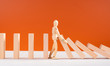 Wooden man stopping falling domino concept. Symbol of crisis, risk, management, leadership and determination. Domino effect. Fall of the crumbling business is saved by mannequin. Orange background.