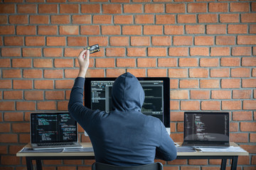 Wall Mural - computer hacker or cyber attack concept, dangerous hooded hacker using multiple computers typing bad