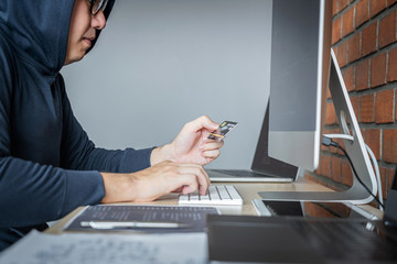Wall Mural - computer hacker or cyber attack concept, dangerous hooded hacker using multiple computers typing bad