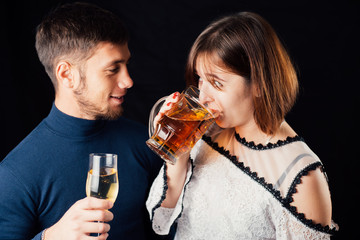 A man and a woman on a black background, a woman drinking beer and a man drinking champagne is a stereotypical activity