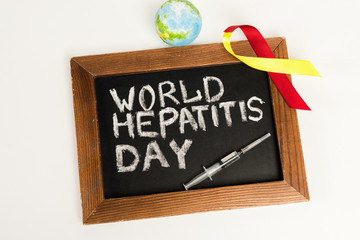 top view of chalkboard with world hepatitis day lettering near ribbon, globe and syringe isolated on white