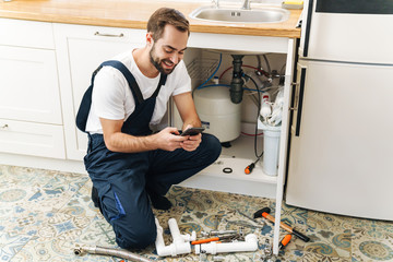 Man plumber work in uniform indoors using mobile phone.