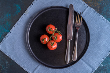 Small bunch of ripe fresh tomatoes and cutlery on black plate ,flat lay.