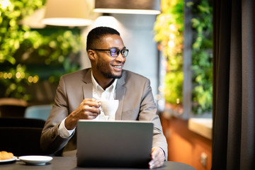 Wall Mural - Black guy holding cup of coffee looking through window