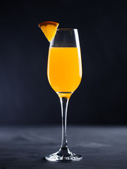 Wall Mural - glass of fizzy mimosa cocktail champagne with orange juice on a dark background
