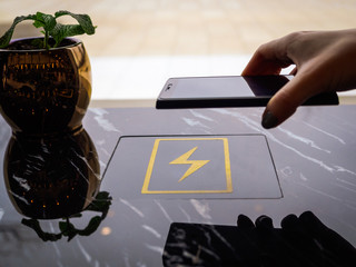 A girl charges her smartphone using a wireless charging station in a public place. A woman charges her phone and uses modern technologies. Discharged smartphone in women's hands