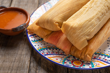 Mexican tamales with red sauce on wooden background