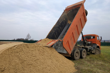 A large orange dump truck unloads the sand