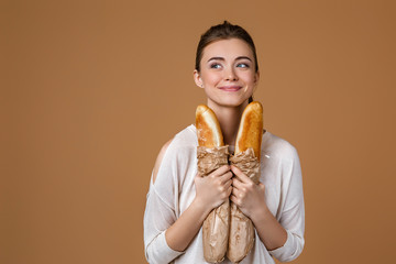 Portrait of beautiful smiling young woman holding paper bag with bread on studio yellow background. girl with paper bag with fresh fragrant long loaf. copy space