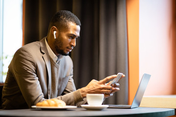 Wall Mural - Portrait of afro guy in earphones using cellphone and computer