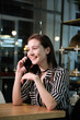 © Oleg Samoylov - Stylish young beautiful smiling girl in a striped shirt and black dress is sitting at a table in a cafe and talking on the phone.