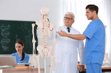 Canvas Print - Medical students and professor studying human skeleton anatomy in classroom