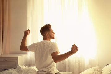 Canvas Print - Young man stretching on bed at home, view from back. Lazy morning