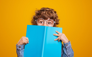 Funny schoolboy hiding behind textbook