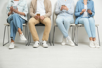 People with modern smartphones sitting on chairs indoors, closeup