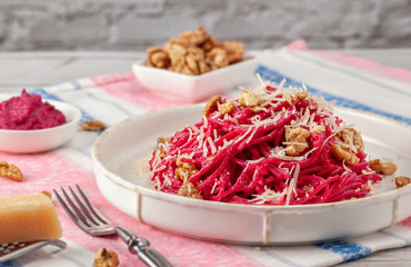 Wall Mural - Spaghetti with beetroot pesto sauce, walnuts and parmesan on a light background