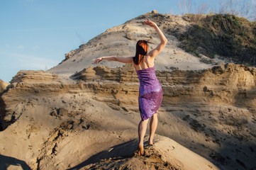 Brown-haired woman in purple glittering dress dancing on sand