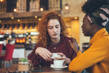 A young woman is talking with a female friend about her problem in a cafe. The friend is supportive and understanding.