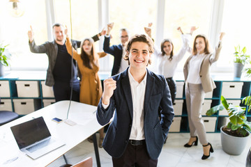 Wall Mural - Handsome businessman with win gesture standing in front of his colleagues in office