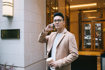 Adult ethnic entrepreneur with takeaway hot drink phoning on street