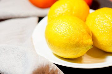 Three fresh yellow lemons lie on a white plate on a grey linen background. Selective focus. Close up.