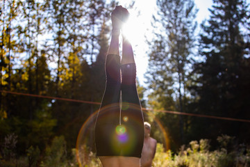 Poster - A closeup view on the legs and feet of a woman standing upside down, headstand with backlight and lens flare in woodland during mindful yoga in nature. Soft focus shot