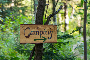 A closeup shot of a handmade wooden sign saying camping with a green arrow pointing right, hanging from a tree in a forest during an earth festival